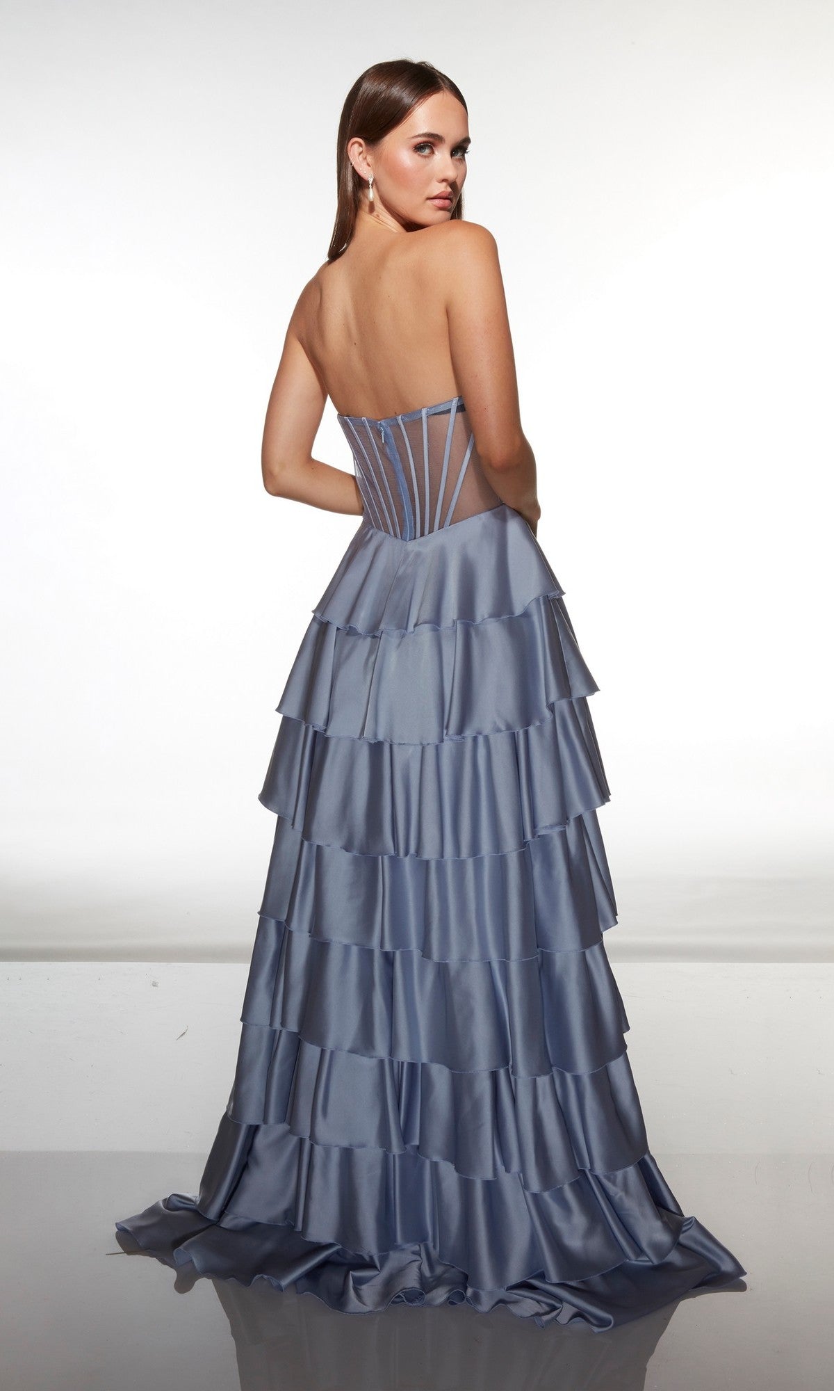 A woman stands facing away, looking over her shoulder in the Long Prom Dress: Alyce 62056—a light blue strapless satin gown with a tiered ruffle A-line skirt—set against a plain white background.
